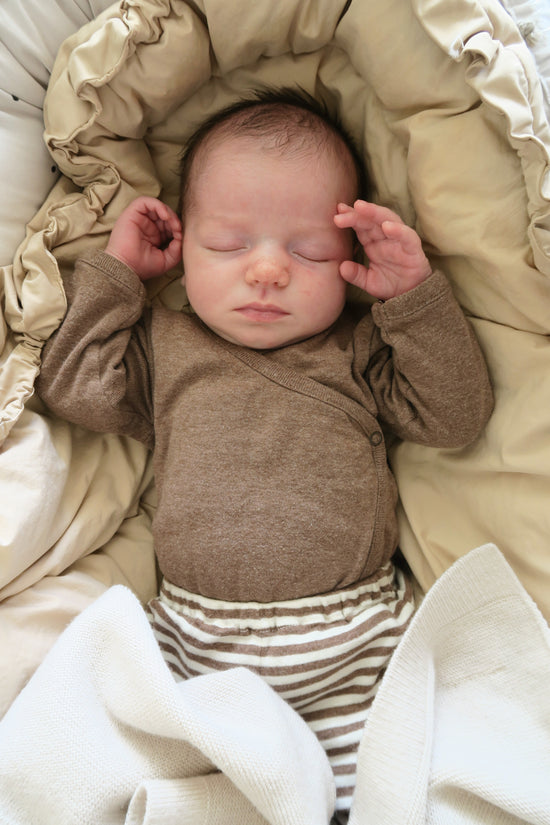 Newborn baby sleeping wearing a brun bodysuit and a stripped white and brun pant from OiOiOi