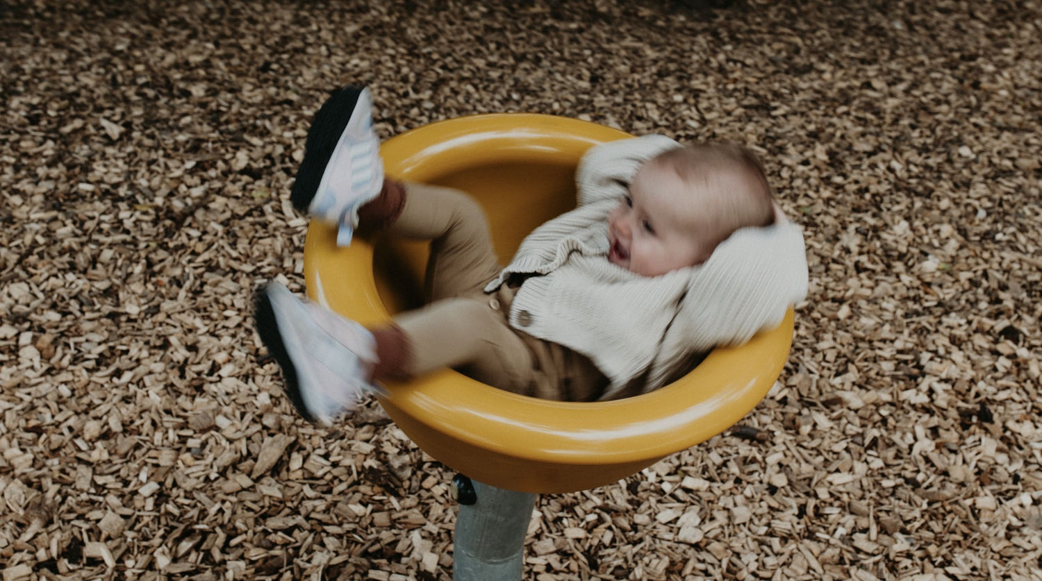 Laughing Baby laying in a yellow bowl wearing brown and beiges organic baby clothes from OiOiOi
