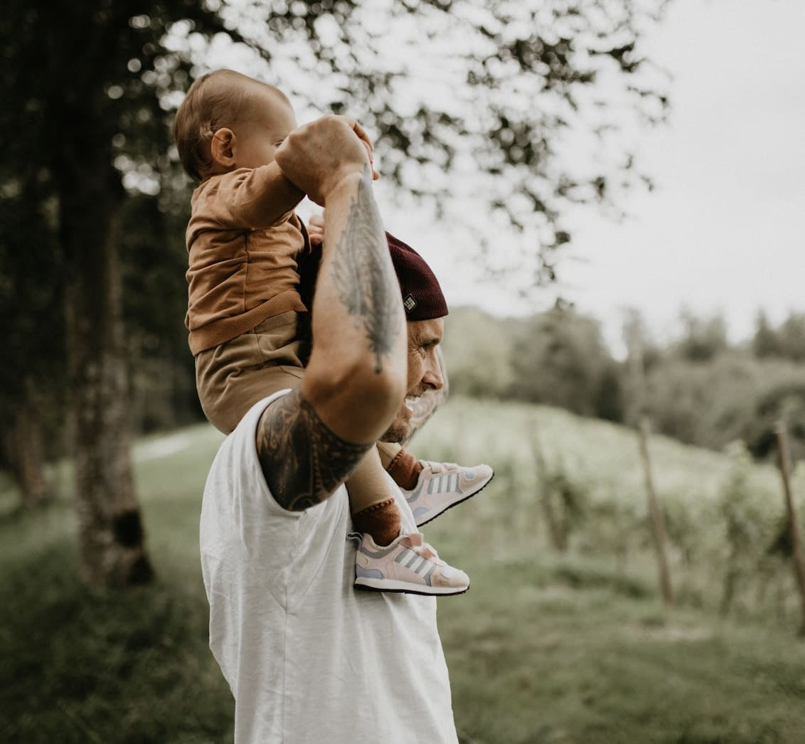 Father with white T-Shirt having child with brownish organic babyclothes on his shoulders