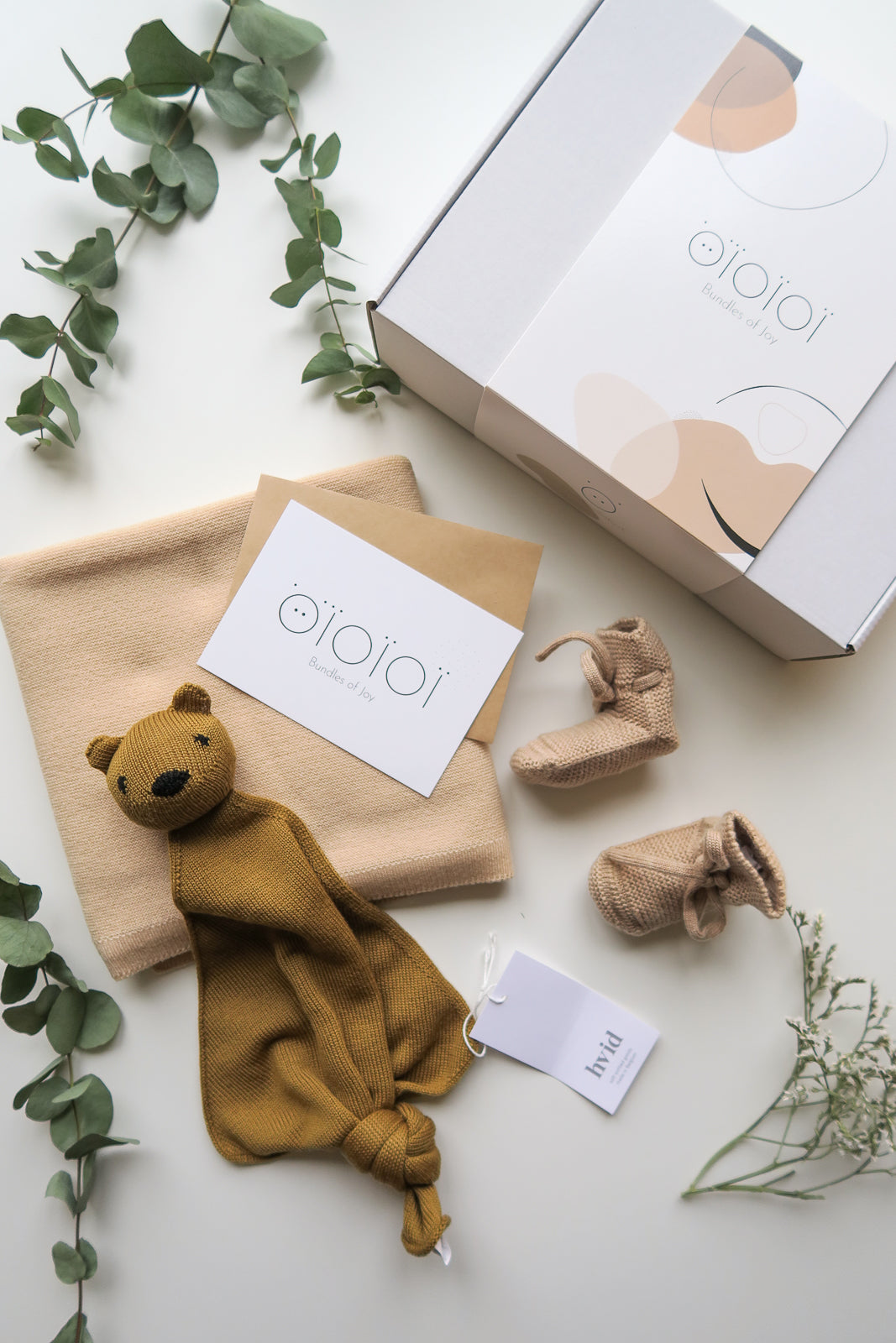 Photography from above: Gift box with OiOiOi gift card, brown cuddly toy, beige socks, lying on white background