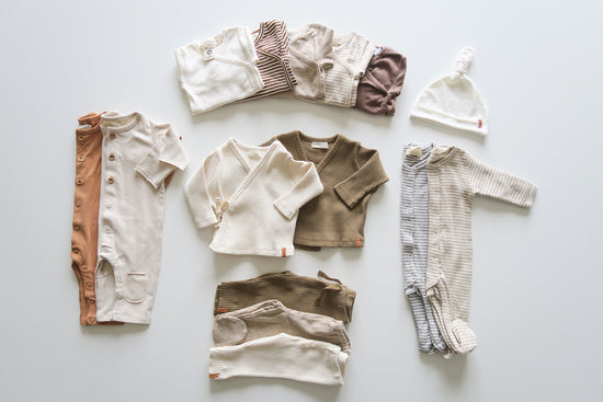Striped beige, white, orange, brun and grey organic baby clothes disposed on a white neutral background