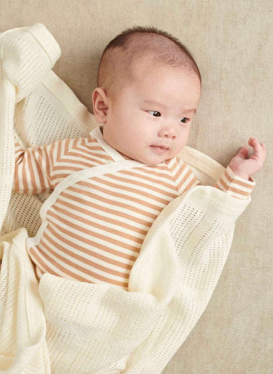 Baby light skin color and a orange and white striped bodysuit made of organic cotton from Mori and lies in a white blanket
