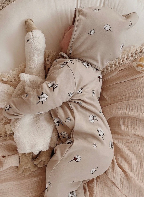 Baby lies sideways asleep with a cuddly duck in it's arms wears beige pajamas from Organic Zoo and OiOiOi with floral pattern