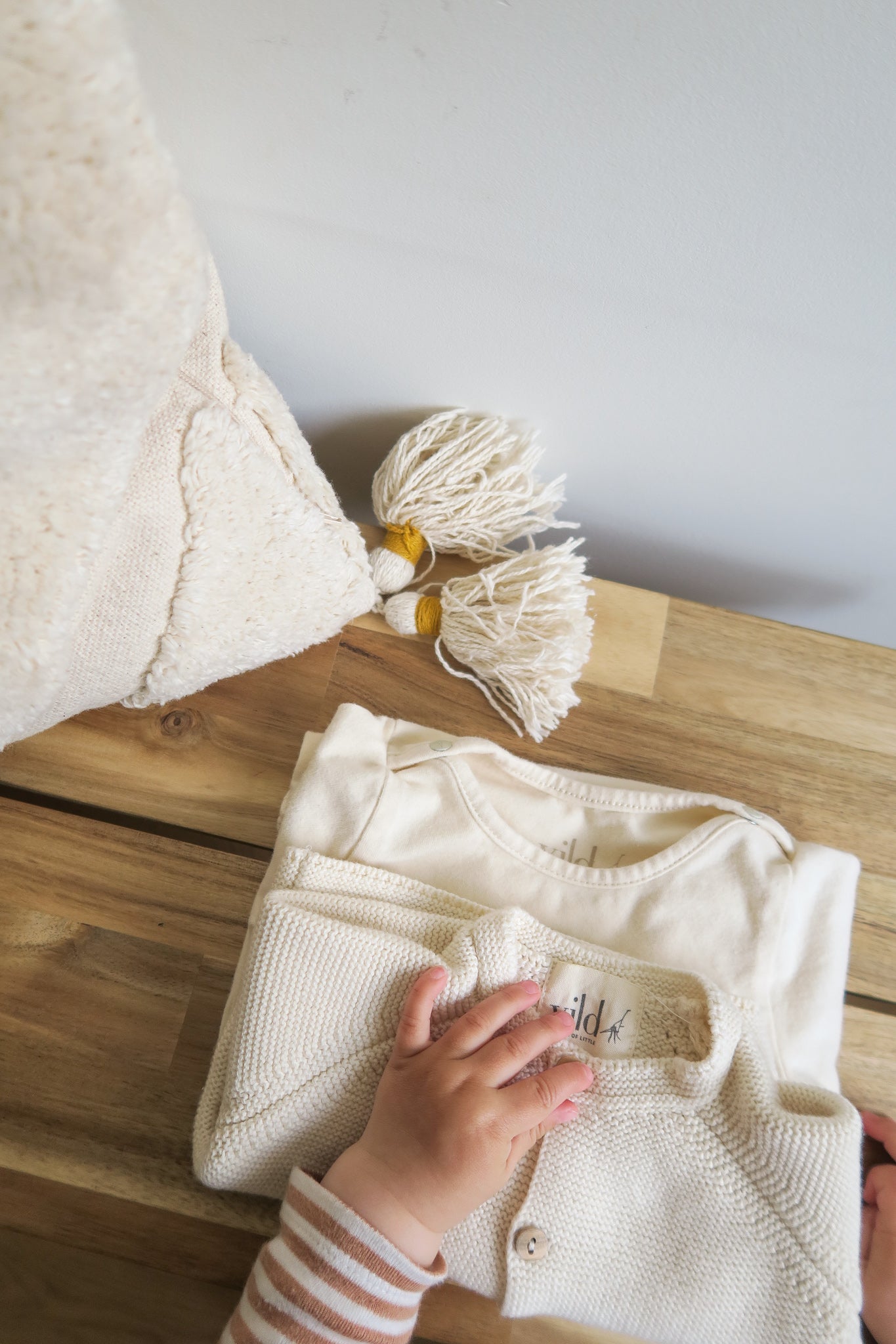 Baby hand lying on two folded organic cotton baby cardigans in light colours from OiOiOi
